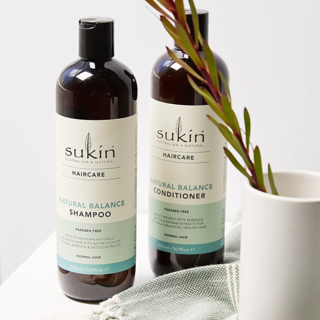 A bottle of Sukin Natural Balance Shampoo for normal hair displayed on a clean, white marble surface with botanical leaves in the background.
