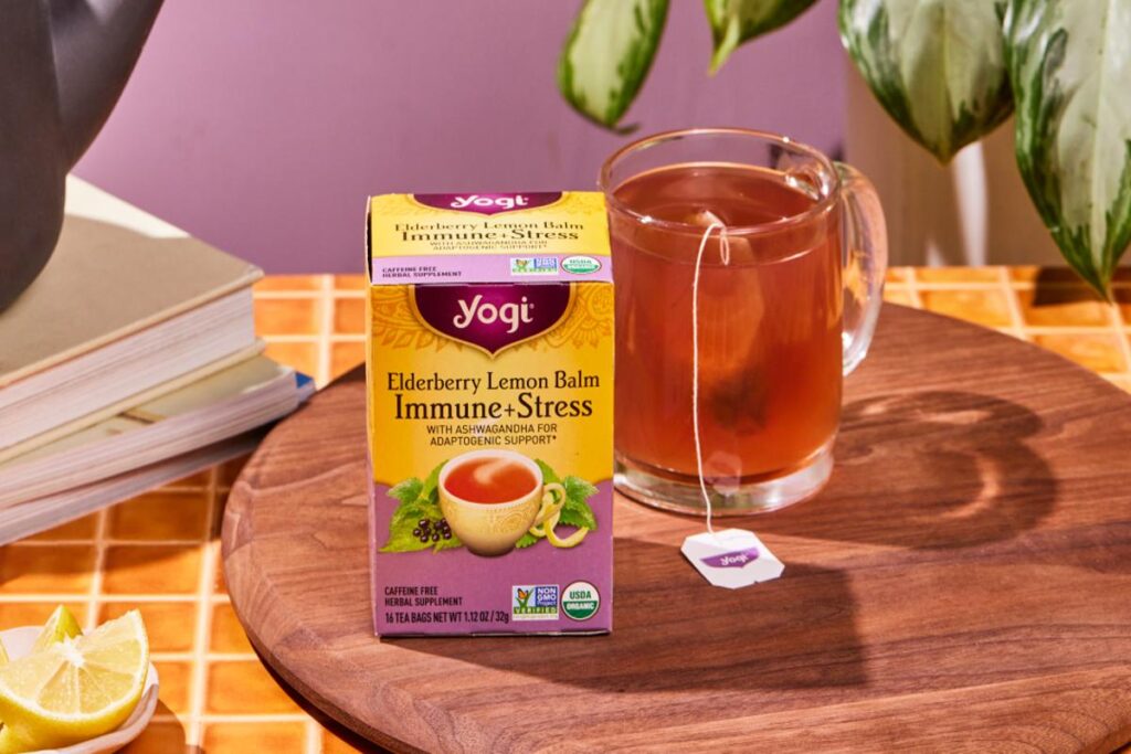 Yogi Elderberry Lemon Balm Immune+Stress tea box with a cup of herbal tea on a wooden table